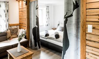 A modern room with wooden walls and an elegant design. Curtains with a deer motif separate the sleeping area from the living room.