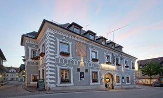 A historic building with a gray facade and decorative elements. There are flower boxes at the windows and a clear evening sky.