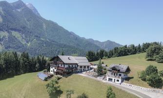 The picturesque Hotel Sonnfeld in the mountains, surrounded by lush greenery. In the background, majestic mountains rise under a clear sky.