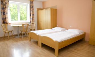 A simple room with two single beds and a table with chairs. The window offers a view of the outside and provides bright light.