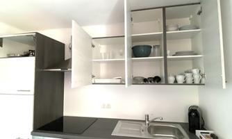 A modern kitchen with dark wooden surfaces and open upper cabinets. The equipment includes a stove, a dishwasher, and a sink.