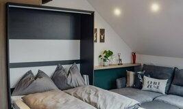 A modern bedroom with a fold-out bed and a cozy seating area. Bright walls and wooden details create an inviting atmosphere.