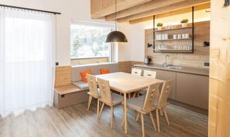 A modern kitchen with a dining area and wooden furniture. The room is bright and inviting, with large windows and a cozy atmosphere.