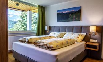 A cozy bedroom with a large bed and pretty bedding. The room has a window overlooking a green landscape and mountains.