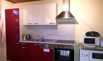 A modern kitchen with red and white cabinets. It is equipped with a stove, a refrigerator, and small kitchen appliances.