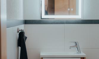 A modern bathroom with an elegant sink and a lighted mirror. A black towel hangs on the wall.