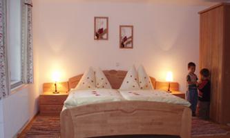 A cozy bedroom with a large bed and warm lighting. In the background, two children are playing.