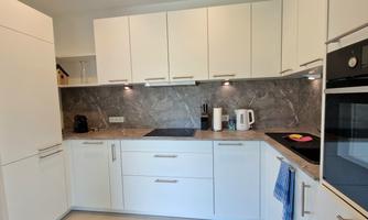 A modern kitchen with white cabinets and gray walls. The countertop is tidy and some kitchen appliances are visible.