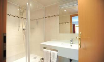 A bright bathroom with a shower, a sink, and a mirror. The walls are brightly tiled, and there is plenty of natural light.