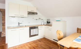 A modern kitchen with light cabinets and a wooden floor. The dining area is simply furnished and offers space for several people.