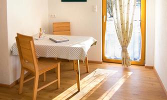 A bright room with a wooden table and chairs. Sunshine streams through the window and illuminates the space.