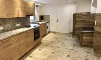 A modern kitchen with wooden cabinets and an elegant tiled floor. It is well-lit and can be used for various cooking activities.