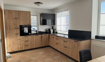 A modern kitchen with wooden fronts and black countertops. The space is bright and spacious with window light.