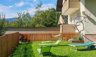 A cozy garden with loungers and a wooden fence. In the background, there are trees and a visible sky.