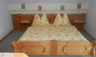A cozy bedroom with a large wooden bed and yellow bedding. The walls are light and subtly decorated.