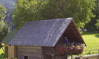 A small, charming wooden house with a blooming flower box. Surrounded by a green meadow and trees in the mountains.