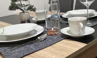 A set table with plates, glasses, and cutlery. In the background, gray chairs and a small Christmas tree are visible.