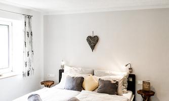 A cozy bedroom with a double bed and soft cushions. Bright walls and wooden elements create a relaxing atmosphere.
