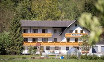A well-maintained building with several floors and balconies. Surrounded by friendly trees and a green meadow.