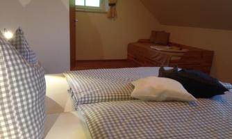 A cozy bedroom with a double bed and an adjacent single bed. The bright walls and daylight create an inviting atmosphere.