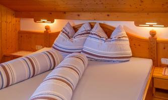 A cozy bedroom with a large bed and several pillows. The walls are made of wood, and there is soft lighting.