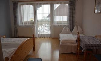 A simple room with two beds, a table, and chairs. Large windows offer a view of the snowy landscape outside.