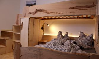 A cozy, modern bedroom with a wooden loft bed and a small seating area. The beds are decorated with checked pillows and a blanket.