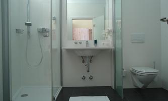 A modern bathroom with a shower and sink. On the right, there is a toilet and a gray floor.