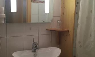 A simple bathroom with a sink and a mirror cabinet. The shower is separated by a curtain.