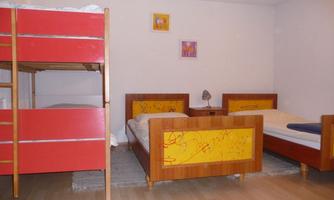 A simple bedroom with a red bunk bed and two single beds. Colorful pictures hang on the walls.