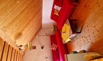 A cozy living space with red sofas and wooden ceilings. On the table lies a yellow tablecloth and there is a lamp on the wall.