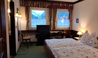 A cozy hotel room with two beds, a television, and a table. The view of the mountains can be seen through the windows.