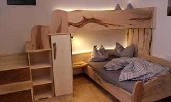 A cozy wooden house bed with a staircase and two pillows. The room has a warm atmosphere with indirect lighting.