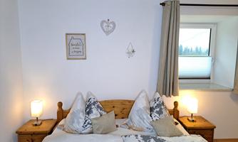 A cozy bedroom with a double bed and pretty bedding. Two nightstands with lamps complement the room, which is brightly lit by a window.