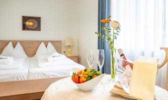 A cozy bedroom with a double bed and fresh flowers. On the table are champagne glasses and a bowl of fresh fruit.