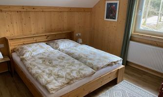 A cozy bedroom with a double bed and wood paneling. The window offers a view of the nature outside.