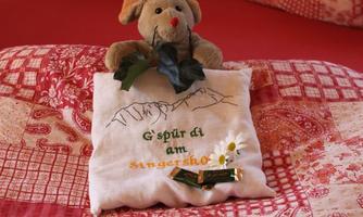 A cozy bedroom with a red bed and decorative pillows. A plush toy sits on a pillow with an embroidered message.
