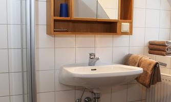 A modern bathroom with a sink and a wooden shelf. Towels and a blue container are also visible.