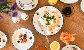 A beautiful breakfast table with various foods. There is yogurt, fruit, rolls, and drinks on plates and cups.