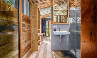 A modern, bright bathroom with wooden paneling and a glass shower. The space is designed to be minimalist and inviting.