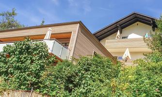A modern house with a balcony, surrounded by a lot of greenery. The sky is clear and sunny.
