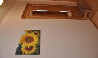 A bright room with a wooden door and a shoe rack. A picture of sunflowers is hanging on the wall.