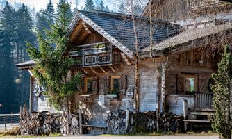 A cozy wooden house in the mountains, surrounded by trees. The facade features traditional details and is surrounded by a green lawn.