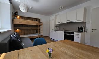 A modern living space with a kitchenette and a dining area. In the background, there is a bunk bed as well as a cozy seating area.