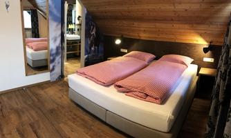 A cozy bedroom with a double bed and striped bedcovers. The wooden walls and the window create a warm atmosphere.