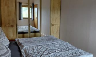 A bedroom with a large bed and a mirror wardrobe. The room has wooden ceilings and a window that lets in light.