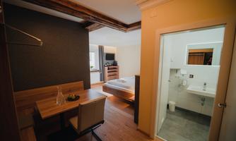A cozy room with a bed, a table, and a chair. In the background, there is a modern bathroom.