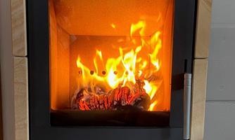 A modern wood stove with a blazing fire. The flames glow in various shades of yellow and orange.