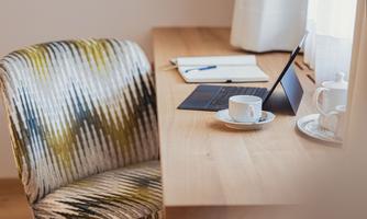 A modern desk with a laptop, a cup of coffee, and a notepad. The chair has a striking design and the room is bright and inviting.