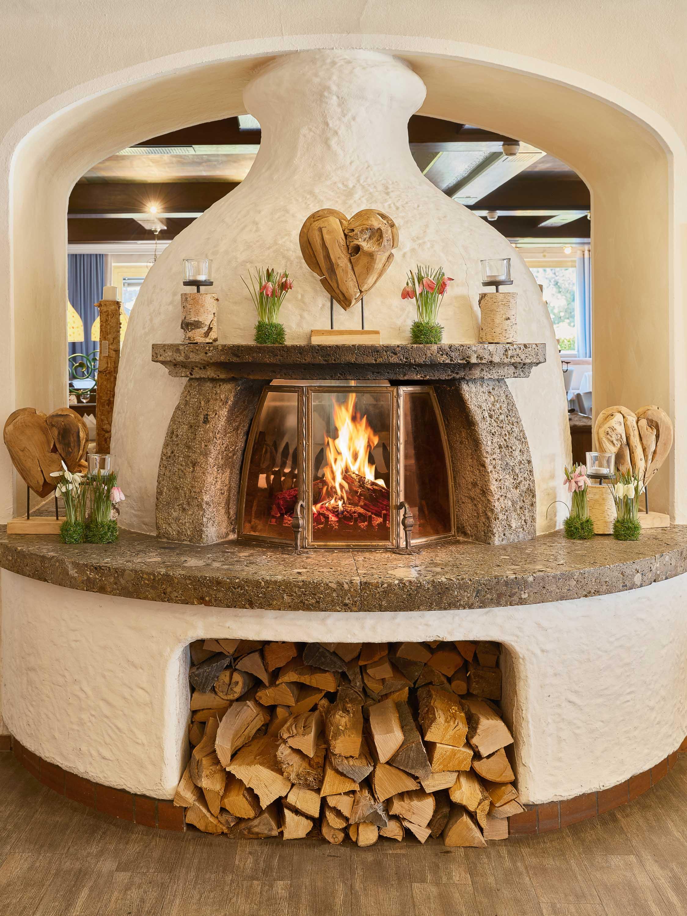 A cozy fireplace in a rustic room, surrounded by wood and decorative elements. The flames create an inviting atmosphere.